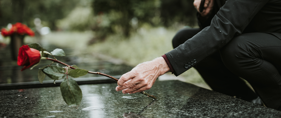 Elegant sad elderly man standing on the rain with umbrella and grieves at the grave